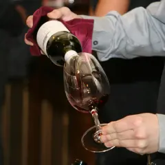 Un serveur verse du vin rouge dans un verre. Le **dépôt de vin blanc** sur la bouteille est visible.