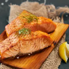 Deux pavés de saumon grillé, ornés d'aneth et de gros sel, servis sur une planche en bois avec des quartiers de citron. Un délice pour accompagner un bon vin.