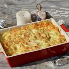 Un plat de gratin de crozet doré et gratiné, prêt à être dégusté. Une bougie et des décorations en bois en forme de cœur complètent la scène hivernale.