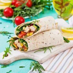 Deux wraps au poulet garnis de légumes frais, servis sur une planche en bois avec des quartiers de citron.