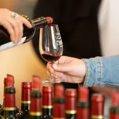 Service d'un vin rouge pour l'apéro, avec des bouteilles alignées en arrière-plan.