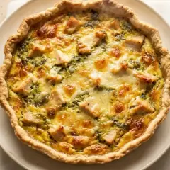 Une délicieuse quiche au poulet, dorée et garnie de morceaux de poulet et de fromage fondant, prête à être dégustée.