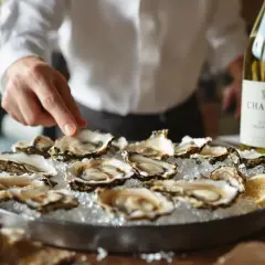 Un serveur présente des huîtres fraîches sur glace, accompagnées d'une bouteille de Chablis. Le choix parfait : quel vin blanc avec les huîtres ?