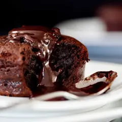 Un fondant au chocolat dégoulinant de sauce, une cuillère prête à savourer ce délice.