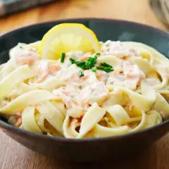 Un plat de tagliatelles au saumon crémeuses, garni d'une tranche de citron et de ciboulette fraîche. Un délice pour les papilles.