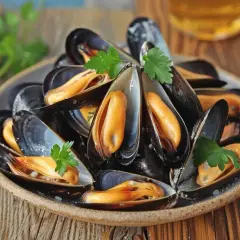 Assiette de moules savoureuses, garnie de persil. La quantité de moules par personne semble généreuse pour un repas délicieux.