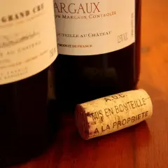 Bouchon de liège marqué "A.O.C. Mis en bouteille à la propriété", près de bouteilles de vin français, dont une de Margaux.