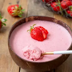 Délicieuse mousse fraise dans une noix de coco, garnie d'une fraise fraîche. Une cuillère dorée en extrait une bouchée aérienne.
