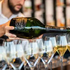 Un serveur verse du champagne d'une bouteille magnum dans plusieurs flûtes. La quantité de champagne est généreuse.