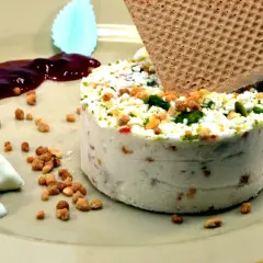 Un délicieux nougat glacé, parsemé de fruits secs et de pistaches, servi avec une touche de coulis de fruits rouges et une gaufrette croustillante.