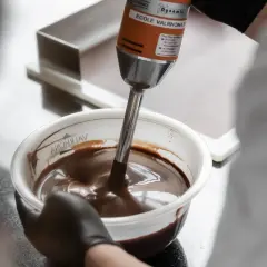 Un mixeur plongeant prépare une onctueuse ganache chocolat dans un bol.