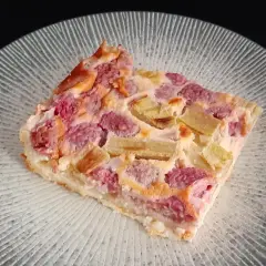Tranche de clafoutis rhubarbe aux fruits rouges, sur une assiette transparente aux motifs rayonnants.