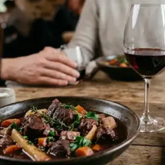 Un plat de sanglier en sauce, garni d'herbes, servi avec un verre de vin rouge et une bouteille de Cahors. Parfait pour savoir quel vin avec sanglier en sauce.
