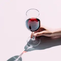Une main tient délicatement un verre de vin rouge, le pouce et l'index sur le pied. Apprenez comment tenir un verre de vin pour en apprécier toutes les saveurs.