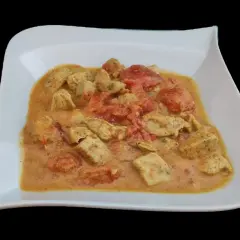 Un plat de poulet curry coco crémeux avec des morceaux de poulet tendre et des tomates, servi dans une assiette blanche.