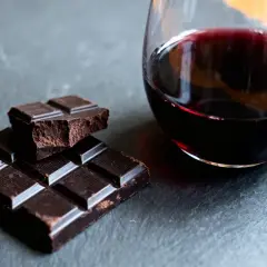 Un verre de vin rouge et des carrés de chocolat noir sur une surface sombre. Un délice pour les sens, le vin et chocolat.