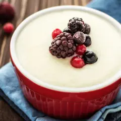 Un bol rouge de semoule au lait crémeuse, garni de baies des bois glacées. Un délice simple et réconfortant.