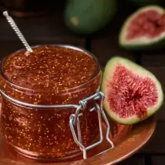 Un bocal de confiture de figues maison, avec des figues fraîches coupées en deux à côté.