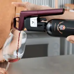 Un appareil Coravin sert un vin rouge d'une bouteille ouverte dans un verre, assurant sa conservation.