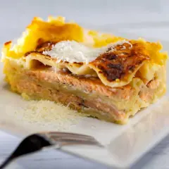 Une part généreuse de lasagne saumon, dorée au four, garnie de parmesan râpé et accompagnée d'un quartier de citron.