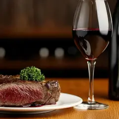 Une succulente entrecôte saignante, garnie d'une touche de persil, accompagnée d'un verre de vin rouge et d'une bouteille.