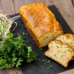 Un délicieux cake au thon, doré et moelleux, tranché et présenté avec du persil frais sur une planche d'ardoise.