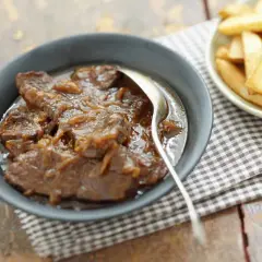 Un plat de carbonade flamande mijotée, servie dans un bol avec une cuillère, à côté d'une coupelle de frites dorées.