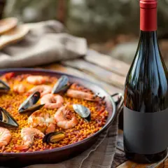 Paella au poulet et fruits de mer, prête à être dégustée avec un vin rouge. Quel vin avec paella poulet fruits mer ? Ce plat coloré appelle un vin fruité.