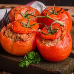 Quatre tomates farcies appétissantes, garnies d'une farce savoureuse, reposent sur une planche en bois rustique.