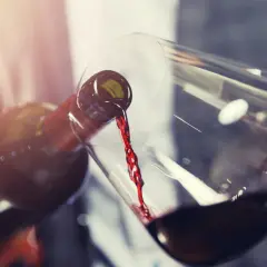 Un vin rouge acide est versé d'une bouteille dans un verre. La lumière dorée illumine la scène.