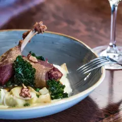 Un plat de cuisse de canard confite, servi avec des légumes verts croquants et une purée onctueuse. Un verre de vin rouge à proximité suggère un accord parfait.