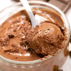 Une cuillère prélève une portion aérienne de mousse au chocolat, garnie de copeaux de chocolat. Un délice gourmand.