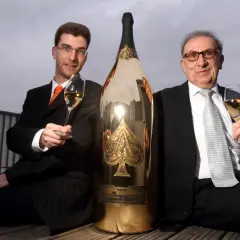 Deux hommes en costume célèbrent avec une gigantesque bouteille de champagne dorée, une véritable bouteille Midas.