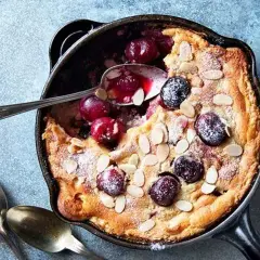 Clafoutis aux cerises dans une poêle, saupoudré de sucre glace et d'amandes effilées. Une recette clafoutis facile et gourmande.