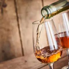 Un verre se remplit d'un vin paillé ambré, un autre verre est déjà servi. Ambiance chaleureuse sur fond de bois.