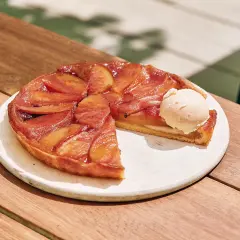 Tarte Tatin aux pommes caramélisées avec une boule de glace à la vanille sur une assiette blanche.