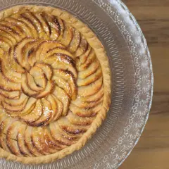 Une magnifique tarte aux pommes, aux pommes caramélisées disposées en spirale sur une pâte dorée, servie sur un plat en verre décoré.