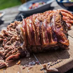 Un morceau de porc rôti avec une couenne croustillante et un effiloché de porc savoureux sur une planche en bois.