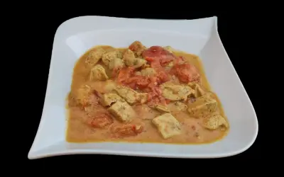 Un plat de poulet curry coco crémeux avec des morceaux de poulet tendre et des tomates, servi dans une assiette blanche.