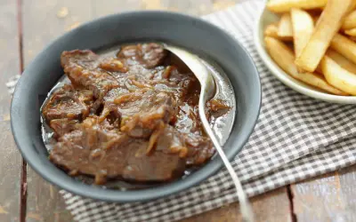 Un plat de carbonade flamande mijotée, servie dans un bol avec une cuillère, à côté d'une coupelle de frites dorées.