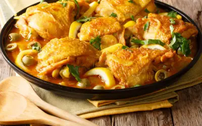 Un plat de poulet aux olives, citron et herbes fraîches, servi dans un plat noir avec des cuillères en bois.
