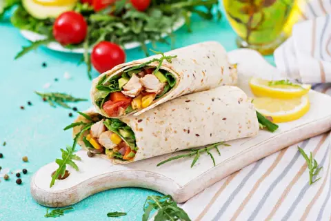 Deux wraps au poulet garnis de légumes frais, servis sur une planche en bois avec des quartiers de citron.