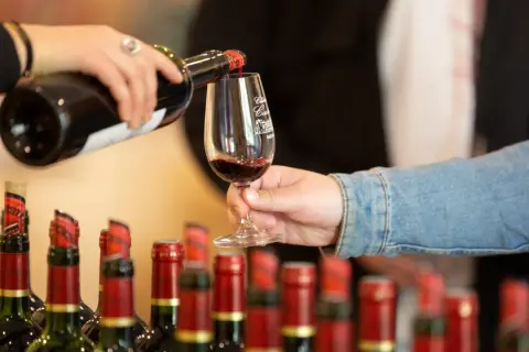 Service d'un vin rouge pour l'apéro, avec des bouteilles alignées en arrière-plan.