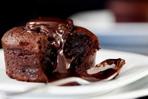 Un fondant au chocolat dégoulinant de sauce, une cuillère prête à savourer ce délice.
