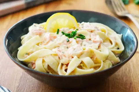 Un plat de tagliatelles au saumon crémeuses, garni d'une tranche de citron et de ciboulette fraîche. Un délice pour les papilles.
