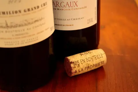 Bouchon de liège marqué "A.O.C. Mis en bouteille à la propriété", près de bouteilles de vin français, dont une de Margaux.