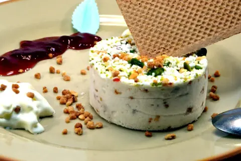 Un délicieux nougat glacé, parsemé de fruits secs et de pistaches, servi avec une touche de coulis de fruits rouges et une gaufrette croustillante.