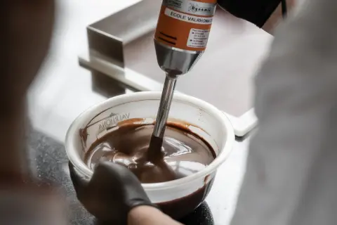 Un mixeur plongeant prépare une onctueuse ganache chocolat dans un bol.