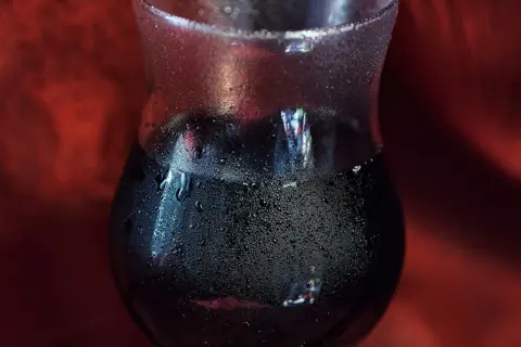 Verre de vin rouge givré, fraîchement sorti du frigo. Les gouttelettes d'eau perlent sur le verre, promettant une dégustation rafraîchissante.
