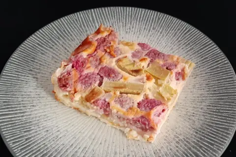 Tranche de clafoutis rhubarbe aux fruits rouges, sur une assiette transparente aux motifs rayonnants.